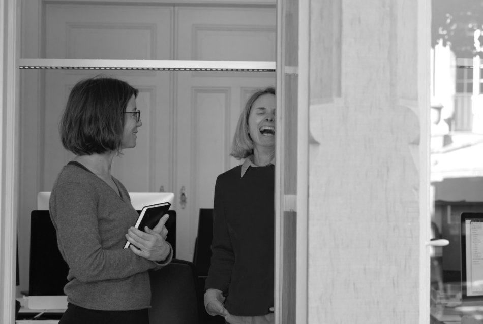 Zwei weibliche Mitarbeiter unterhalten sich und lachen im Büro
